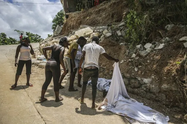 People look at the body of a person who died during the earthquake, on the road to Camp-Perrin, Les Cayes, Haiti, Sunday, August 15, 2021. A 7.2 magnitude earthquake struck Haiti on Saturday, with the epicenter about 125 kilometers (78 miles ) west of the capital of Port-au-Prince, the US Geological Survey said. (Photo by Joseph Odelyn/AP Photo)