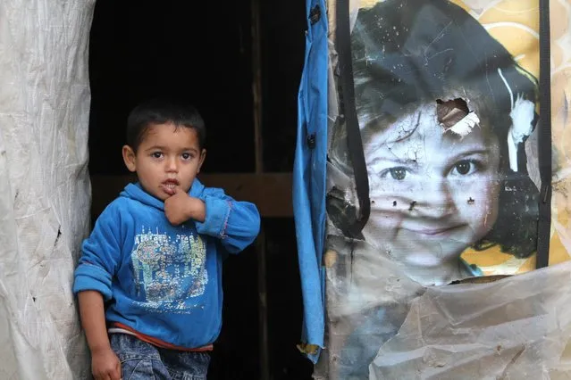 A Syrian boy stands in the entrance of his tent as he watches the visiting of the United Nations High Commissioner for Refugees (UNHCR) Antonio Guterres, during his visit to an informal seaside camp, in the southern costal town of Sarafand, Lebanon, Tuesday, April 14, 2015. (Photo by Mohammed Zaatari/AP Photo)