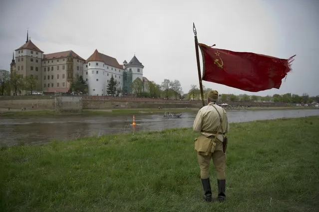 A member of a historical re-enactment group dressed as a Soviet Army soldier stands on the eastern bank of the river Elbe river looking towards Schloss Hartenfels (Castle Hartenfels) on the western side, as he takes part in Elbe Day celebrations, in Torgau, Germany April 25, 2015. (Photo by Stefanie Loos/Reuters)
