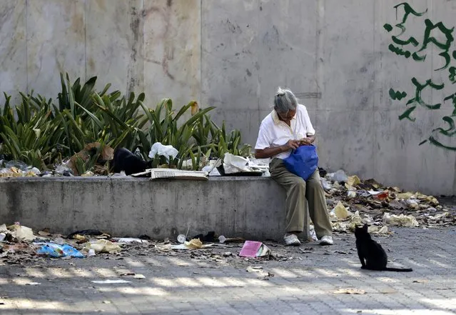 A woman sits on a concrete planter surrounded by litter, in Caracas, Venezuela, Tuesday, March 26, 2019. Much of Venezuela remains without electricity as a new power outage spread across the country. (Photo by Natacha Pisarenko/AP Photo)