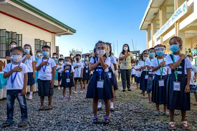 Elementary students wear facemasks and face shields as preventive measure against COVID-19, as they attend a flag-raising ceremony before the start of classes at Longos Elementary School on November 15, 2021 in Alaminos, Pangasinan province, Philippines. After almost two years since schools closed due to the COVID-19 pandemic, the Philippines resumed limited face-to-face classes in 100 schools across the country on November 15. The Philippines is the last country in the world to reopen schools since the pandemic began, after Venezuela reopened schools on October 25. Critics are blaming the government's lackluster pandemic response for the prolonged closure of schools. (Photo by Ezra Acayan/Getty Images)