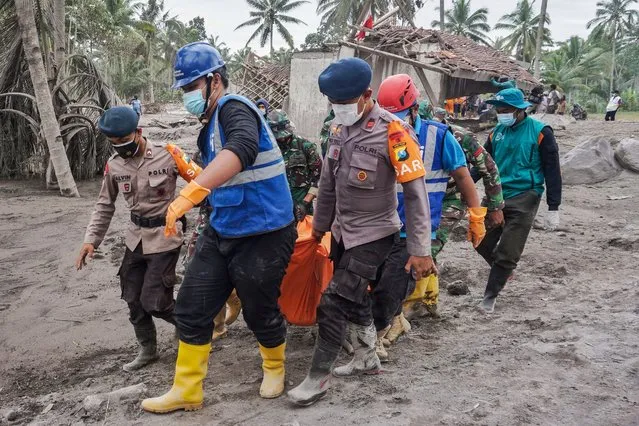 Rescuers carry the body of a victim at an area affected by the eruption of Mount Semeru in Lumajang, East Java, Indonesia, 06 December 2021. The volcano erupted on 04 December, killing at least 14 people and leaving dozens of others injured. (Photo by Ammar/EPA/EFE)