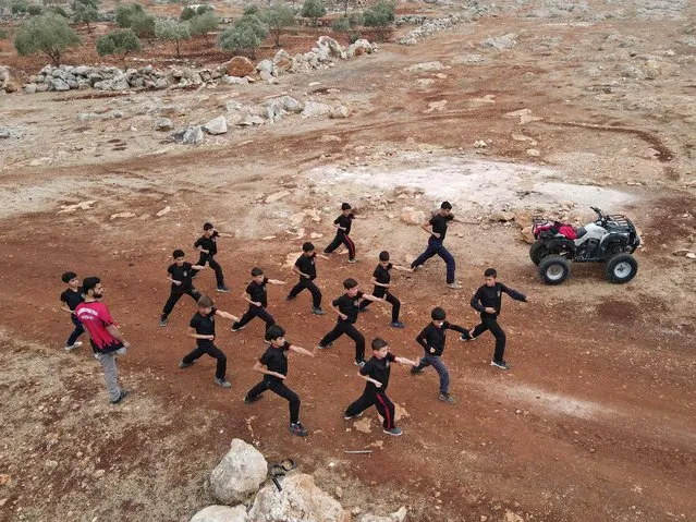 Fadel Othman, a Syrian 24-year-old amputee kung-fu teacher, and his young students perform in an area near his martial arts school in the rebel-held town of Abzimu in the western countryside of Aleppo province on November 25, 2021. Othman was hit by an artillery shell in 2015, during fighting between rebels and government forces in Aleppo. As a result, the young man who started his kung-fu training at the age of 12, braced to forgo his life-long passion. But over the course of the three years he spent in Turkey for medical treatment, he continued classes with martial arts trainers and even participated in several tournaments. (Photo by Aaref Watad/AFP Photo)