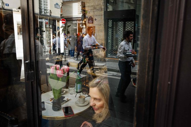 Waiters and waitresses in work outfits reflect in a cafe window as they compete in a traditionnal “Course des cafes” (the cafes' race), in central Paris, on March 24, 2024. Around 200 participants gathered to compete in the 2km race around Paris' Marais district single-handedly carrying a tray bearing a coffee, a glass of water and a croissant. Founded in 1914, this is the first edition of the race after a 13-year hiatus. (Photo by Dimitar Dilkoff/AFP Photo)