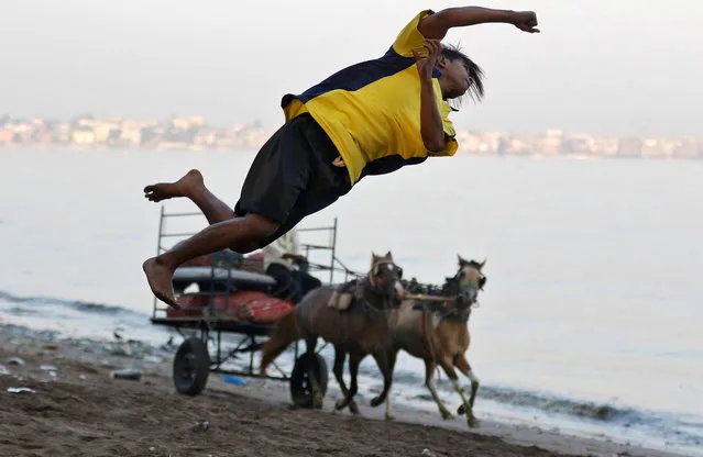 A boy somersaults past a horse-driven cart on a beach along the Arabian sea in Mumbai, India March 6, 2017. (Photo by Shailesh Andrade/Reuters)