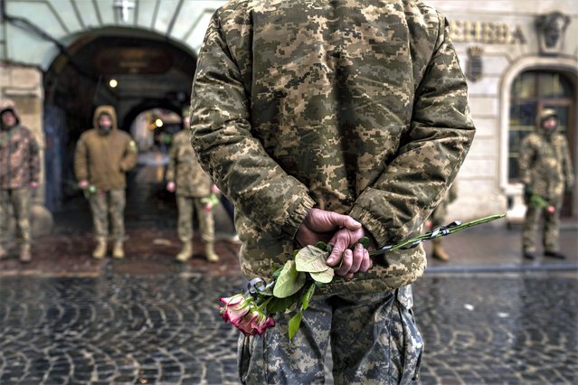Soldiers hold roses at their commander's funeral outside the Holy Apostles Peter and Paul Church in Lviv, western Ukraine, on Tuesday, February 21, 2023. Commander Oleh Voitiuk was injured near Bakhmut and died in a hospital in Lyman Ukraine. (Photo by Petros Giannakouris/AP Photo)