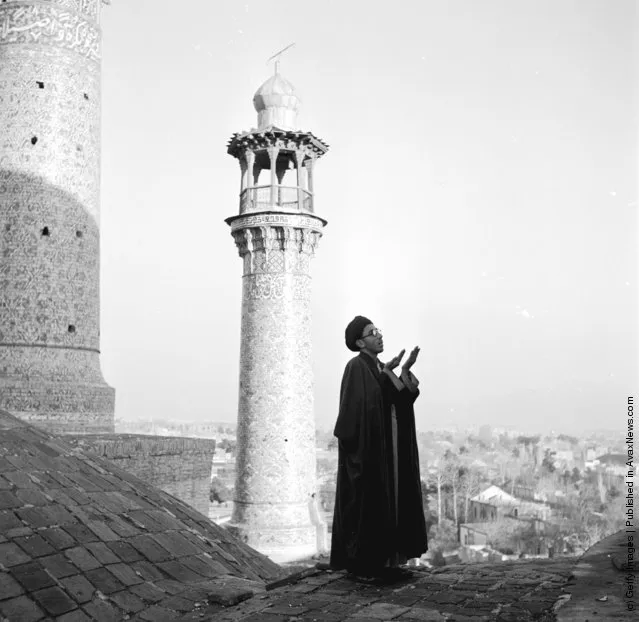 1952:  Standing on a rooftop a muezzin is calling the faithful to prayer. Behind him rises a minaret