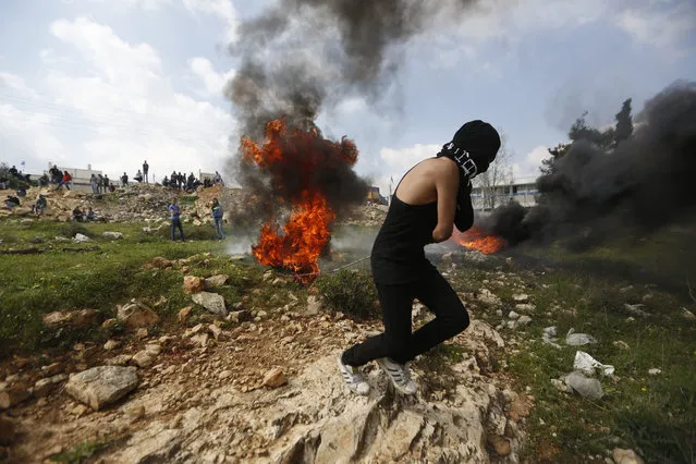 A Palestinian protester moves a burning tyre during clashes with Israeli troops after the funeral of Mahmoud Hattab, 17, at the Jalazoun refugee camp near the West Bank city of Ramallah, Friday, March 24, 2017. The Palestinian Health Ministry said Israeli troops killed the 17-year-old and wounded another three when soldiers opened fire on their car in the West Bank. The Israeli military said the men had exited their vehicle near a Jewish settlement and “hurled fire bombs” at the community. It said the soldiers fired at the attackers, who fled the scene in their vehicle. (Photo by Majdi Mohammed/AP Photo)