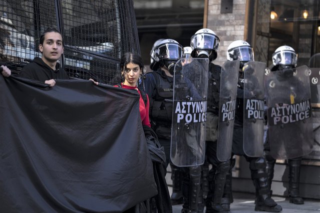 University students hold a black banner as they stand next to riot police quarding the headquarters of private operator Hellenic Train, in Athens, Friday, March 3, 2023. Demonstrators marched through the city center to protest the deaths of dozens of people late Tuesday, in Greece's worst recorded rail accident. (Photo by Petros Giannakouris/AP Photo)