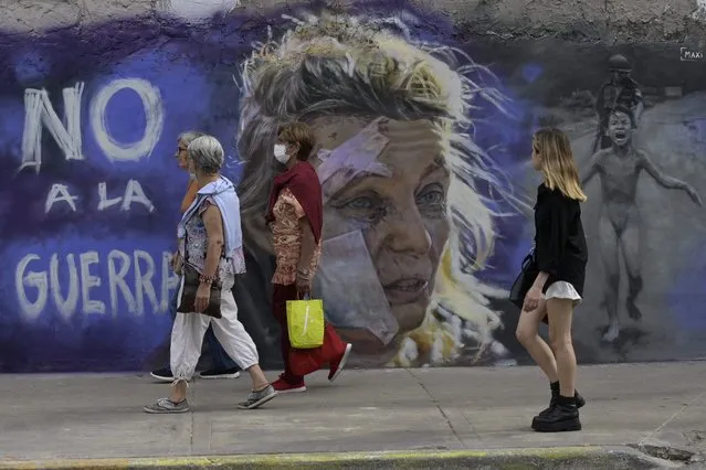 Women walk pass the mural “No to war” by muralist Maximiliano Bagnasco in Buenos Aires on March 5, 2022. Bagnasco paint this mural against the war inspired by two iconic images the portrait of Helena (C), a 53-year-old teacher standing outside a hospital after the bombing of the eastern Ukraine town of Chuguiv on February 24, 2022, as Russian armed forces invade Ukrain taken by AFP Greek photojournalist Aris Messinis and Kim Phuc Phan Thi, also known as “Napalm Girl”, the iconic 1972 Vietnam War photograph taken by Nick Ut of AP. (Photo by Juan Mabromata/AFP Photo)