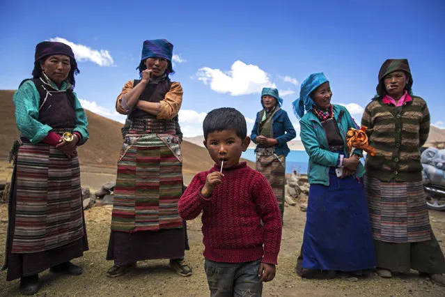 A child eats a lollipop as Tibetan women stand in a village near the Yamdrok Lake on April 26, 2017 in Dongla County in the Lhokha Prefecture of Tibet Autonomous Region, China. Yamdrok Lake is one of the four largest sacred lakes in Tibet. The lake is surrounded by many snow-capped mountains and is fed by numerous small streams. (Photo by Wang He/Getty Images)