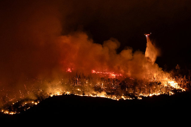 A helicopter drops water over the Thompson wildfire as firefighters continue battling fire into the night near Oroville, California on July 3, 2024. (Photo by Carlos Barria/Reuters)