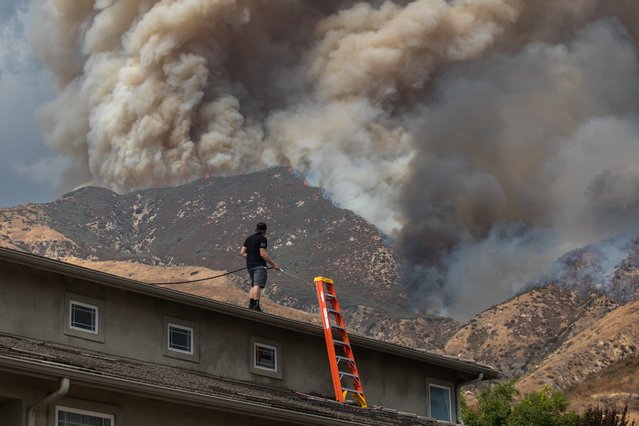 A man waters the roof of his home to protect the house as the Line Fire burns in the foothills of the San Bernardino Mountains, forcing evacuations for neighborhoods on September 7, 2024 in San Bernardino, California. The fire started on Thursday afternoon and spread to more than 3900 acres as of this afternoon with zero containment. (Photo by Apu Gomes/Getty Images)