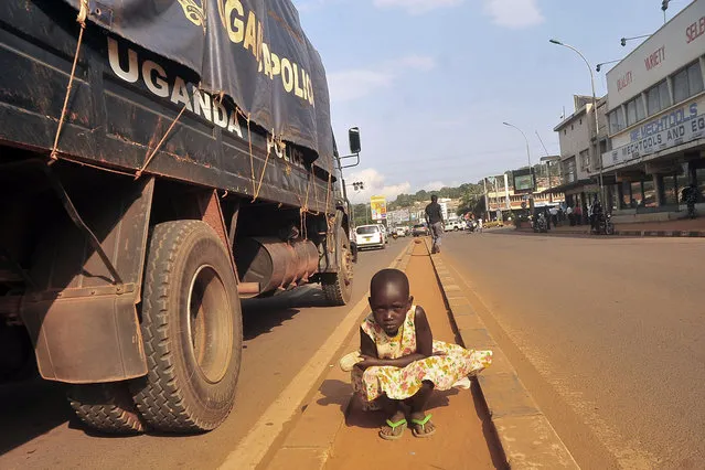 A Ugandan street child poses in the middle of the streets as a police truck goes past her, in Kampala, Uganda, Thursday, July 17, 2014. Homeless children in Uganda's urban centers face beatings and abuse at the hands of police and local officials, Human Rights Watch charged in a new report that urges Ugandan authorities to protect street children from targeted roundups and arbitrary detentions. A police spokesman said the allegations are “totally not true”. (Photo by Stephen Wandera/AP Photo)