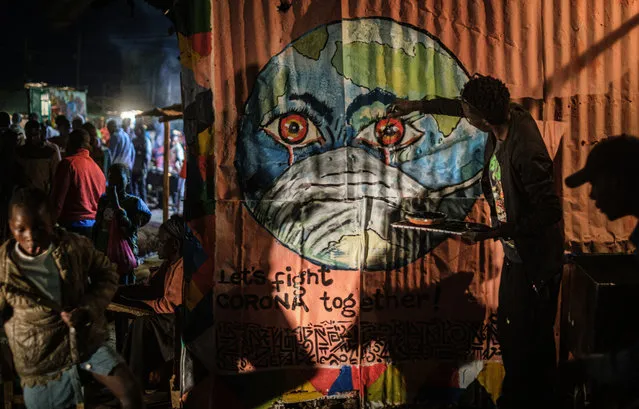 Kenyan visual artist Grandsan paints graffiti, that shows the earth wearing a mask, to increase awareness of the prevention against the COVID-19 coronavirus at a butcher shop in Kibera, Kenya, on March 23, 2020. (Photo by Yasuyoshi Chiba/AFP Photo)