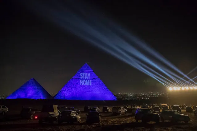 A picture taken on April 18, 2020 show the Great pyramids lighten-up with blue light and reading with a laser projection the message “Stay Home” on the Giza plateau outside the Egyptian capital of Cairo, on the world heritage day, as the country fights against the spread of the COVID-19, (the novel coronavirus). (Photo by Khaled Desouki/AFP Photo) 