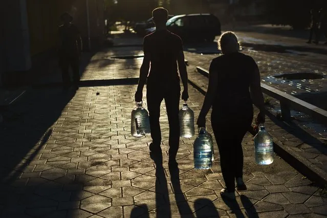 A couple carry water bottles after filling them up in a store in Pokrovsk, Donetsk region, eastern Ukraine, Thursday, August 4, 2022. (Photo by David Goldman/AP Photo)