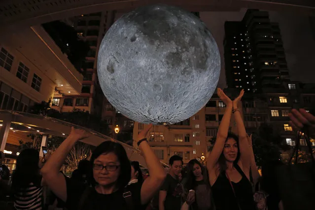 Visitors pose for photographs in front of an installation “Museum of the Moon”, a giant seven-meter-wide glowing sculpture of the moon, created by British artist Luke Jerram in Hong Kong to celebrate the Mid-Autumn Festival, Wednesday, October 4, 2017. (Photo by Kin Cheung/AP Photo)