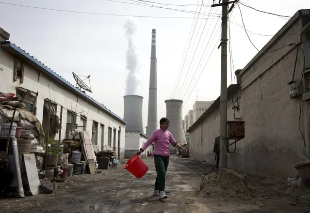 In this April 12, 2013 file photo, a woman walks through a neighborhood near a coal-fired power plant in Beijing. (Photo by Andy Wong/AP Photo)