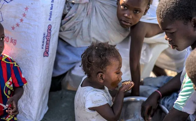 A child eats a handful of grain from a pot at the Hugo Chavez public square transformed into a refuge for families forced to leave their homes due to clashes between armed gangs in Port-au-Prince, Haiti, Thursday, October 20, 2022. (Photo by Ramon Espinosa/AP Photo)