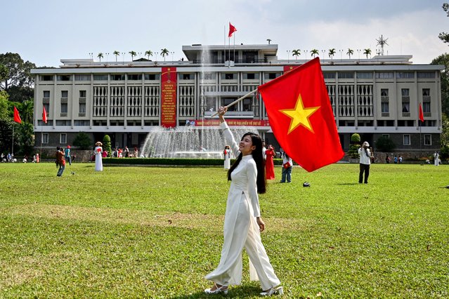 A woman poses with a Vietnamese flag in front of the Reunification Palace in Ho Chi Minh City on April 28, 2025, ahead of celebrations to mark the 50th anniversary of the end of the Vietnam War. (Photo by Nhac Nguyen/AFP Photo)