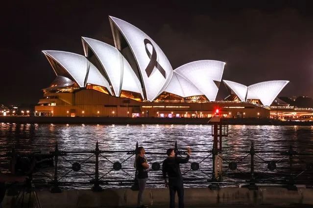 People stand in front of a black ribbon, symbolising remembrance and mourning, being projected onto the Sydney Opera House on February 9, 2023 in solidarity with Turkey and Syria after a massive earthquake devastated the two countries. (Photo by David Gray/AFP Photo)