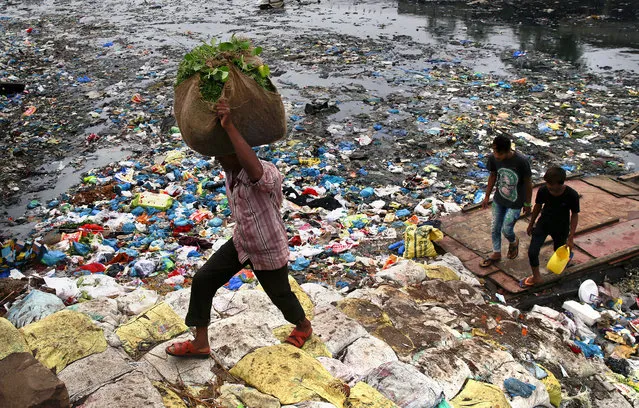 A man carries a sack of vegetables as he walks past a polluted canal littered with plastic bags and other garbage in Mumbai, India, Sunday, October 2, 2016. (Photo by Rafiq Maqbool/AP Photo)