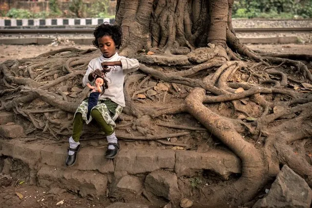 A girl child plays with a doll sitting under a tree at a roadside, in Guwahati, in Indian northeastern state of Assam, Friday, February 10, 2023. In India, the legal marriageable age is 21 for men and 18 for women. Poverty, lack of education, and social norms and practices, particularly in rural areas, are considered reasons for child marriages across the country. UNICEF estimates that at least 1.5 million girls under 18 get married in India every year, making it home to the largest number of child brides in the world, accounting for a third of the global total. (Photo by Anupam Nath/AP Photo)