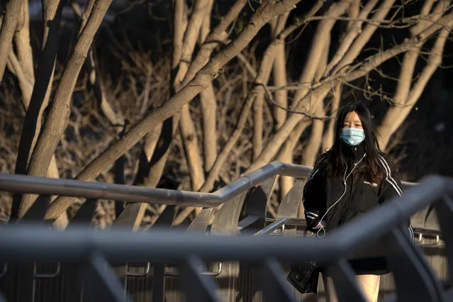 A woman wearing a face mask to protect against the spread of the coronavirus walks along a street during the morning rush hour in Beijing, Wednesday, December 30, 2020. Beijing has urged residents not to leave the city during the Lunar New Year holiday in February, implementing new restrictions and mass testings after several coronavirus infections last week. (Photo by Mark Schiefelbein/AP Photo)