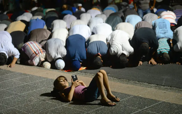 Call to Prayer. A young girl plays on her phone in front of Muslim men as they take evening prayer in Lakemba. (Photo by Jeremy Piper/Australian Life Prize 2015)