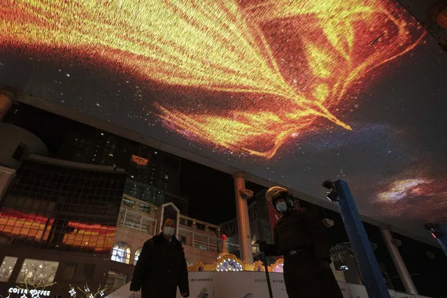 A security guard stands on duty as a phoenix is shown on a giant screen on New Year Eve in Beijing Thursday, December 31, 2020. This New Year's Eve is being celebrated like no other, with pandemic restrictions limiting crowds and many people bidding farewell to a year they'd prefer to forget. (Photo by Ng Han Guan/AP Photo)