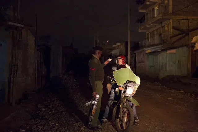 A police officer inspects the identification papers of a motorcyclist carrying a passenger in the neighbourhood of Korogocho during a night patrol in Nairobi, Kenya, October 30, 2015. (Photo by Siegfried Modola/Reuters)