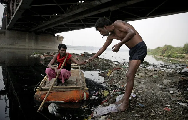 In this photo taken May 28, 2018, Ram Nath, 40, left, who makes a living from recycling trash, receives a bidi from another garbage collector, before going out to look for plastic bottles and other reusable trash through murky waters of Yamuna, India's sacred river that flows through the capital of New Delhi. For more than 25 years, Ram Nath has lived on the banks of the Yamuna River under a 19th-century iron bridge. Each morning, the wiry man walks a few steps from his makeshift hut and enters the black, sludgy waters of one of India’s most polluted rivers. (Photo by Altaf Qadri/AP Photo)