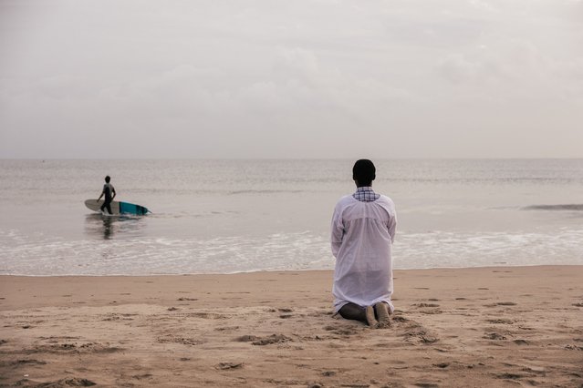 A member of the Shembe Church (R) kneels in prayer as a surfer (L) walks into the ocean on New Year's day in Durban on January 1, 2025. (Photo by Rajesh Jantilal/AFP Photo)