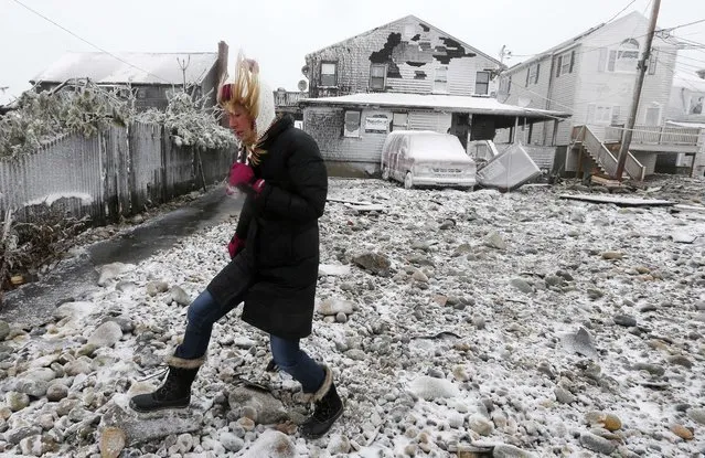 Lynn Leary walks past houses damaged by ocean waves during a winter storm in Marshfield, Mass., Tuesday, January 27, 2015. The storm punched out a section of the seawall in the coastal town of Marshfield, police said. (Photo by Michael Dwyer/AP Photo)