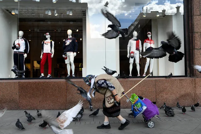 An elderly woman walks past a sports goods shop with pigeons flying around in downtown Moscow on August 8, 2018. The pension age in the country will rise – for the first time in nearly 90 years – by eight years to 63 for women. For men, it will rise by five years to 65 – just two years short of average male life expectancy. (Photo by Kirill Kudryavtsev/AFP Photo)