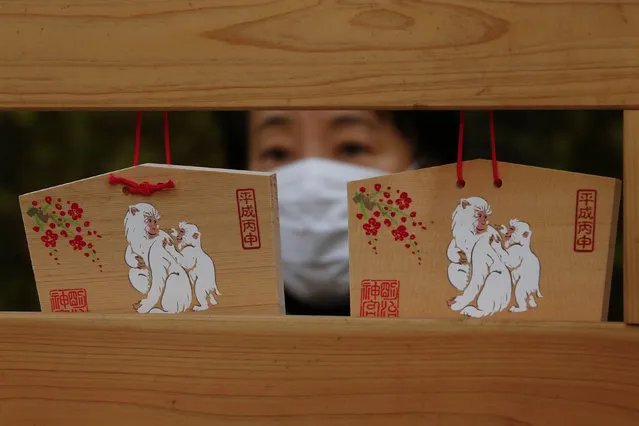 A woman reads an "Ema", a wooden plaque with people's wishes or prayers, during New Year celebrations at the Meiji Shrine in Tokyo, Japan, December 31, 2015. The monkeys on the back of the plaque stand for the zodiac sign for 2016, according to the Chinese calendar. (Photo by Thomas Peter/Reuters)