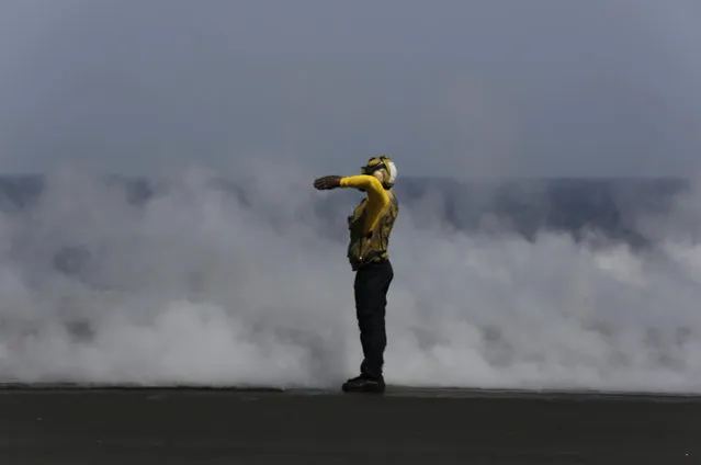A U.S. sailor guides a military jet preparing for takeoff just after another has catapulted off the deck of the USS Carl Vinson aircraft carrier in the Persian Gulf, Thursday, March 19, 2015. (Photo by Hasan Jamali/AP Photo)
