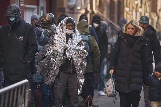 Migrants, left, wait in the cold as they look for a shelter outside a Migrant Assistance Center at St. Brigid Elementary School on Wednesday, November 29, 2023, in New York. (Photo by Andres Kudacki/AP Photo)