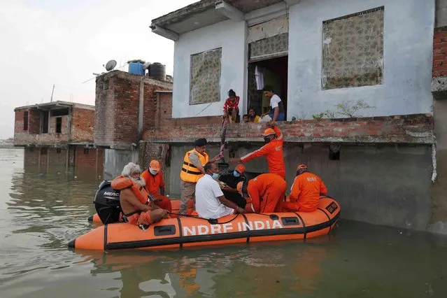 Members of India's National Disaster Response Force (NDRF) distribute food supplies to stranded residents in a submerged area following heavy monsoon rains on the banks of the flooded River Ganges in Prayagraj, India. Friday, August 13, 2021. (Photo by Rajesh Kumar Singh/AP Photo)