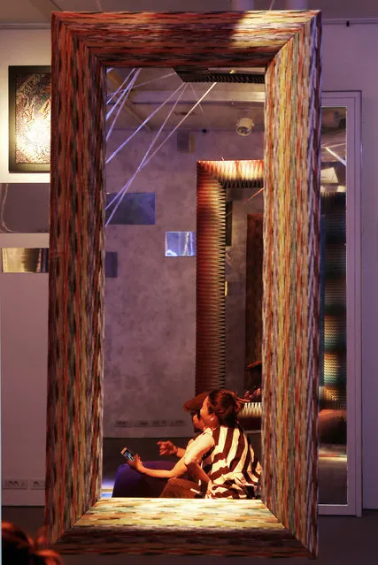 In this picture taken on Wednesday, April 15, 2015 people sit next to a mirror by Missoni at the Milan Furniture Fair, in Milan, Italy. (Photo by Antonio Calanni/AP Photo)