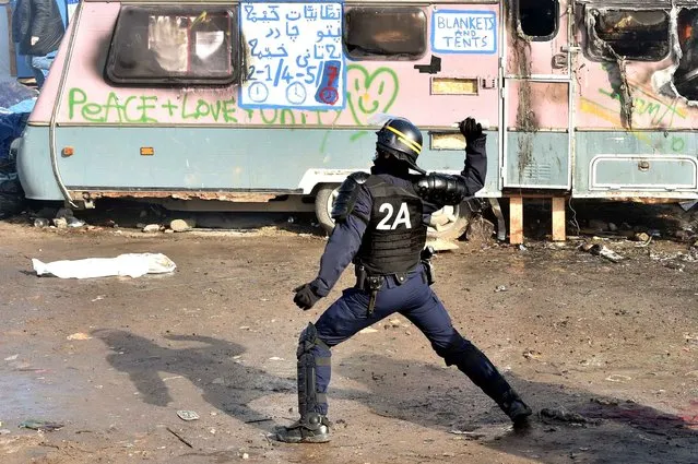 An anti-riot policeman prepares to throw a tear gas canister on February 29, 2016, during the dismantling of half of the “Jungle” migrant camp in the French northern port city of Calais. Two bulldozers and around 20 workers began destroying makeshift shacks, with 30 police cars and two anti-riot vans stationed nearby. (Photo by Philippe Huguen/AFP Photo)