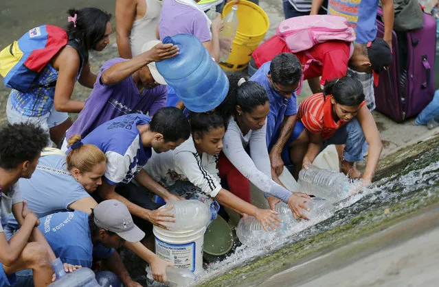 People collect water falling from a leaking pipeline along the banks of the Guaire River during rolling blackouts, which affects access to running water in people's homes, offices and stores, in Caracas, Venezuela, Monday, March 11, 2019. The blackout has intensified the toxic political climate, with opposition leader Juan Guaido blaming alleged government corruption and mismanagement and President Nicolas Maduro accusing his U.S.-backed adversary of sabotaging the national grid. (Photo by Fernando Llano/AP Photo)