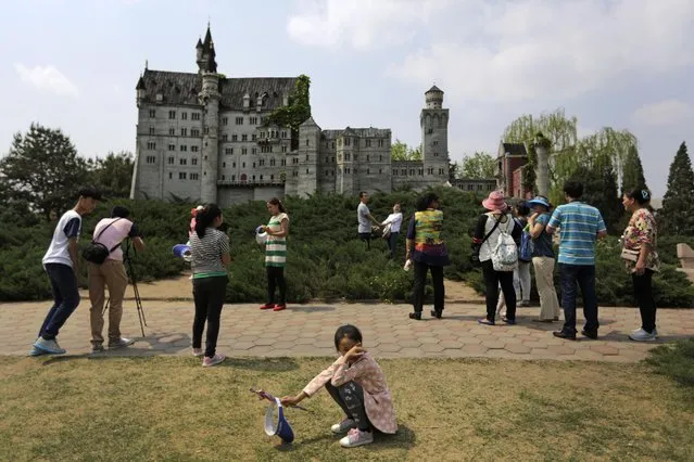 A child rests as visitors take souvenir photos near the replica of Germany's Neuschwanstein Castle at the World Park in Beijing, China, Saturday, May 2, 2015. Millions of Chinese are taking advantage of the May Day holidays to visit popular tourist sites. (Photo by Andy Wong/AP Photo)