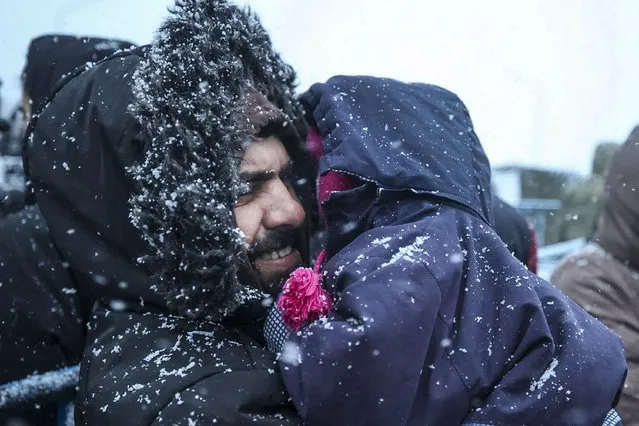 A migrant holds his child as he waits to get meal during a snowfall outside a logistics center at the checkpoint “Kuznitsa” at the Belarus-Poland border near Grodno, Belarus, Tuesday, November 23, 2021. Belarusian authorities say they have helped more than 100 migrants leave the country on Monday and more are prepared to leave Tuesday, a statement that comes after almost two weeks tensions at on the Belarus' border with Poland, where hundreds of migrants remain stuck. (Photo by Leonid Shcheglov/BelTA via AP Photo)