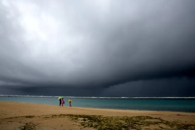 People hold umbrellas as it begins to rain on an otherwise empty beach in Honolulu on Monday, December 6, 2021. A strong storm packing high winds and extremely heavy rain flooded roads and downed power lines and tree branches across Hawaii, with officials warning Monday of potentially worse conditions ahead. (Photo by Caleb Jones/AP Photo)