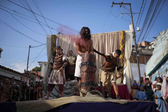 A penitent depicting the role of Jesus Christ is whipped by a fellow devotee playing the role of a Roman soldier, during a Way of the Cross reenactment, as part of Holy Week celebrations in the Petare neighborhood of Caracas, Venezuela, Friday, March 29, 2024. (Photo by Matias Delacroix/AP Photo)