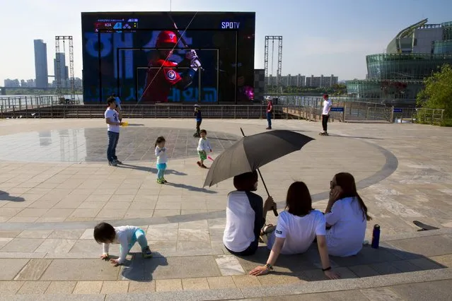Children play in front of a giant TV screen at the embankment of the Han River in Seoul, May 10, 2015. (Photo by Thomas Peter/Reuters)