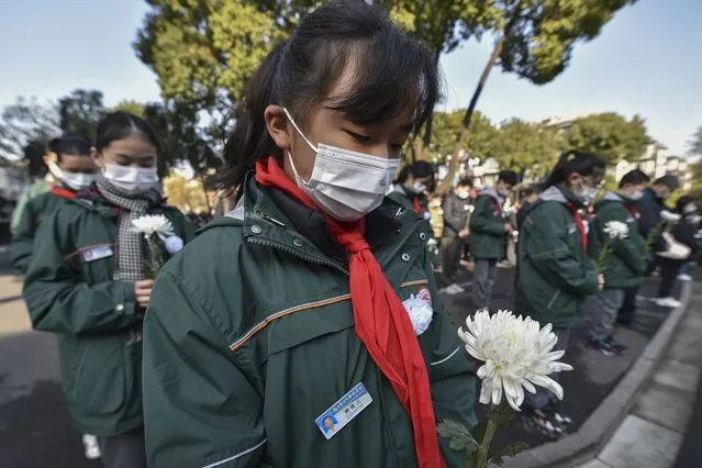 Students wearing face masks hold flowers mourn for the victims of the Nakjing Massacre at a mass burial site during the annual commemoration of the 1937 Nanking Massacre in Nanjing in eastern China's Jiangsu province, Monday, December 13, 2021. (Photo by Chinatopix via AP Photo)