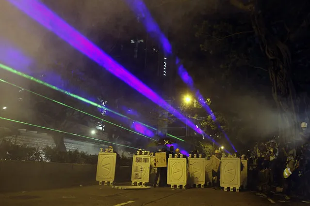 Protesters huddle behind barriers and use laser beams to shine at riot police during confrontation in Tsim Sha Tsui in Hong Kong on Saturday, August 3, 2019. Hong Kong protesters ignored police warnings and streamed past the designated endpoint for a rally Saturday in the latest of a series of demonstrations targeting the government of the semi-autonomous Chinese territory. (Photo by Steve Leung/HK01 via AP Photo)